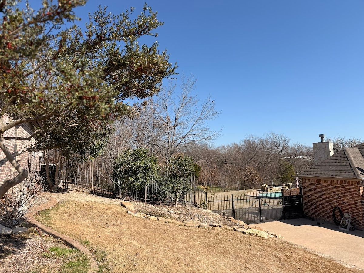 Cleared Fort Worth backyard slope beside an iron pool fence under blue Texas sky
