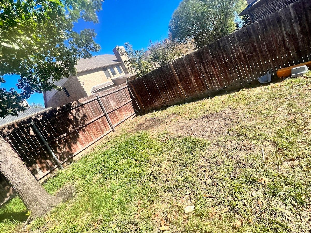Freshly cleaned-up backyard lawn along a wood fence after brush removal in Fort Worth